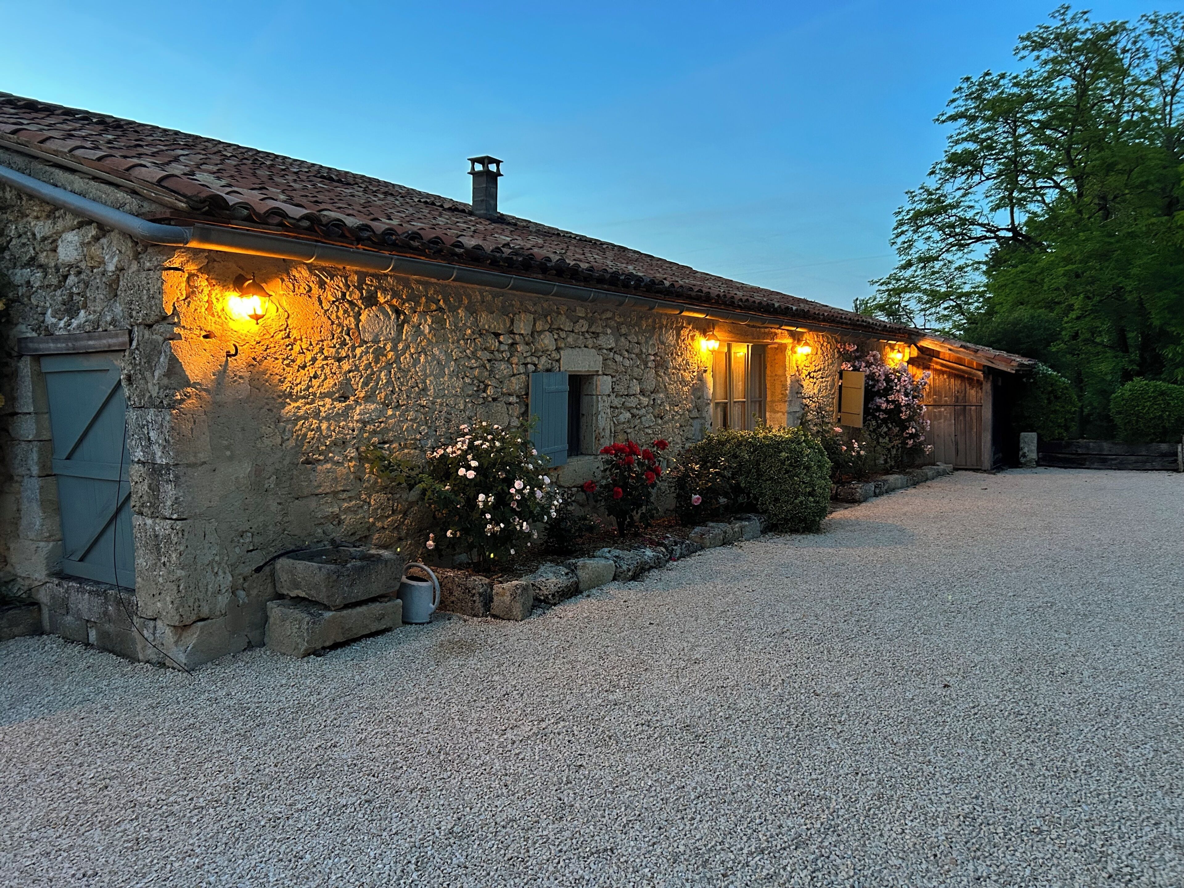 A stone building with a gravel driveway and a garden with flowers.