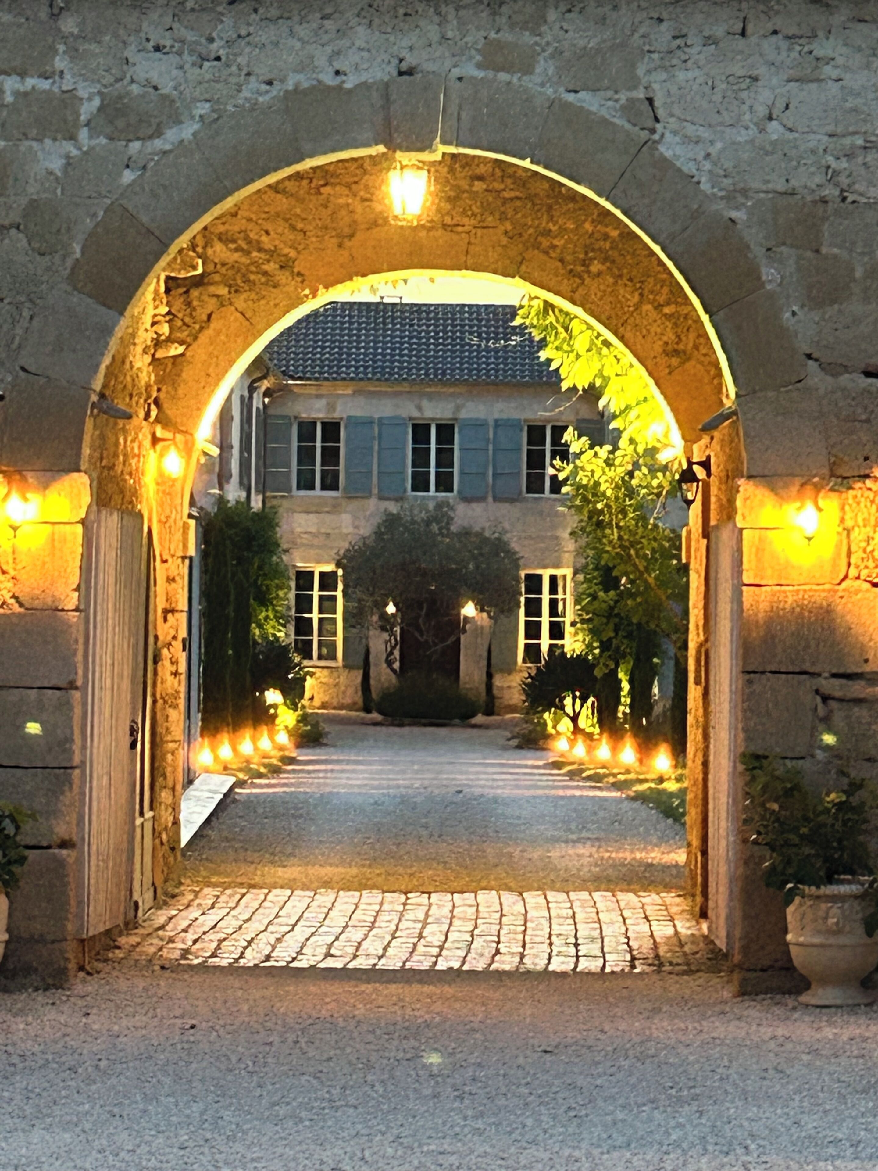 Une entrée en arc de pierre menant à un bâtiment doté d’un toit en tuiles et d’un chemin pavé.