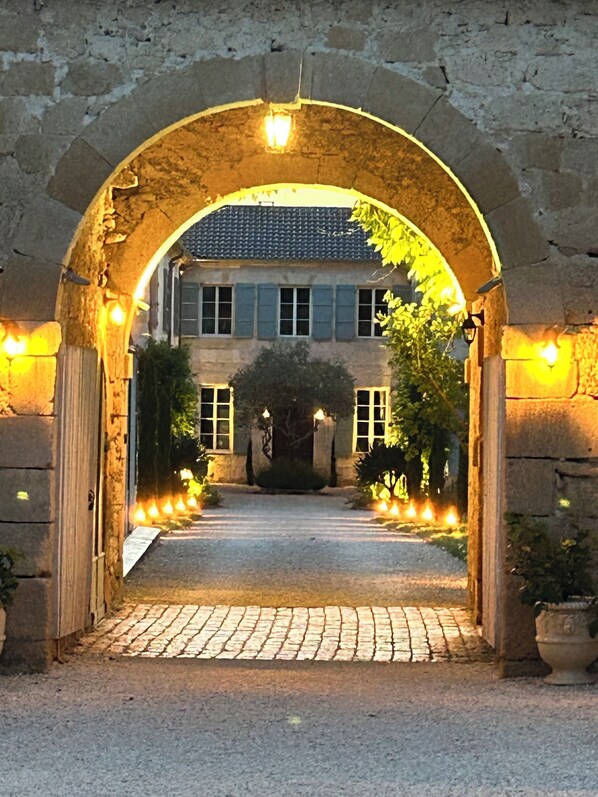 An arched stone entrance leading to a building with a tiled roof and a paved pathway.