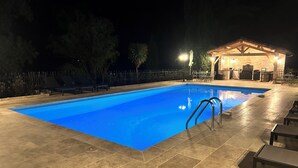 Una piscina con un borde adoquinado, una zona de estar al aire libre techada y una valla.