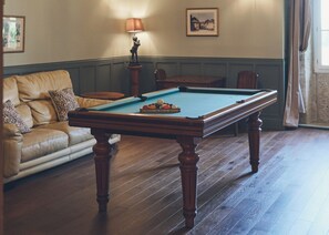 Ein Billardtisch in einem Raum mit einer Couch und einer Lampe.