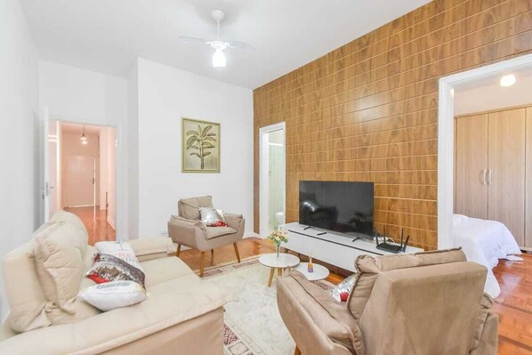Ein modernes Wohnzimmer mit Flachbildfernseher, einer Couch, einem Sessel und einer Wand mit Holzpaneelen.
