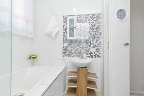 Ein modernes Badezimmer mit einer weißen Badewanne, einem Waschbecken mit Mosaikrückwand und einer Holzwaschtischplatte.