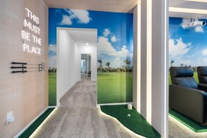 Quarto com mural temático de golfe, um carrinho de golfe e uma área para jogar putting.