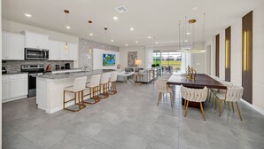 A modern kitchen with white cabinetry, a central island with bar stools, and a dining area with a long table and chairs. - Fabulous Fun 8 Bed Pool Home with Game Room-4297LA (Davenport)