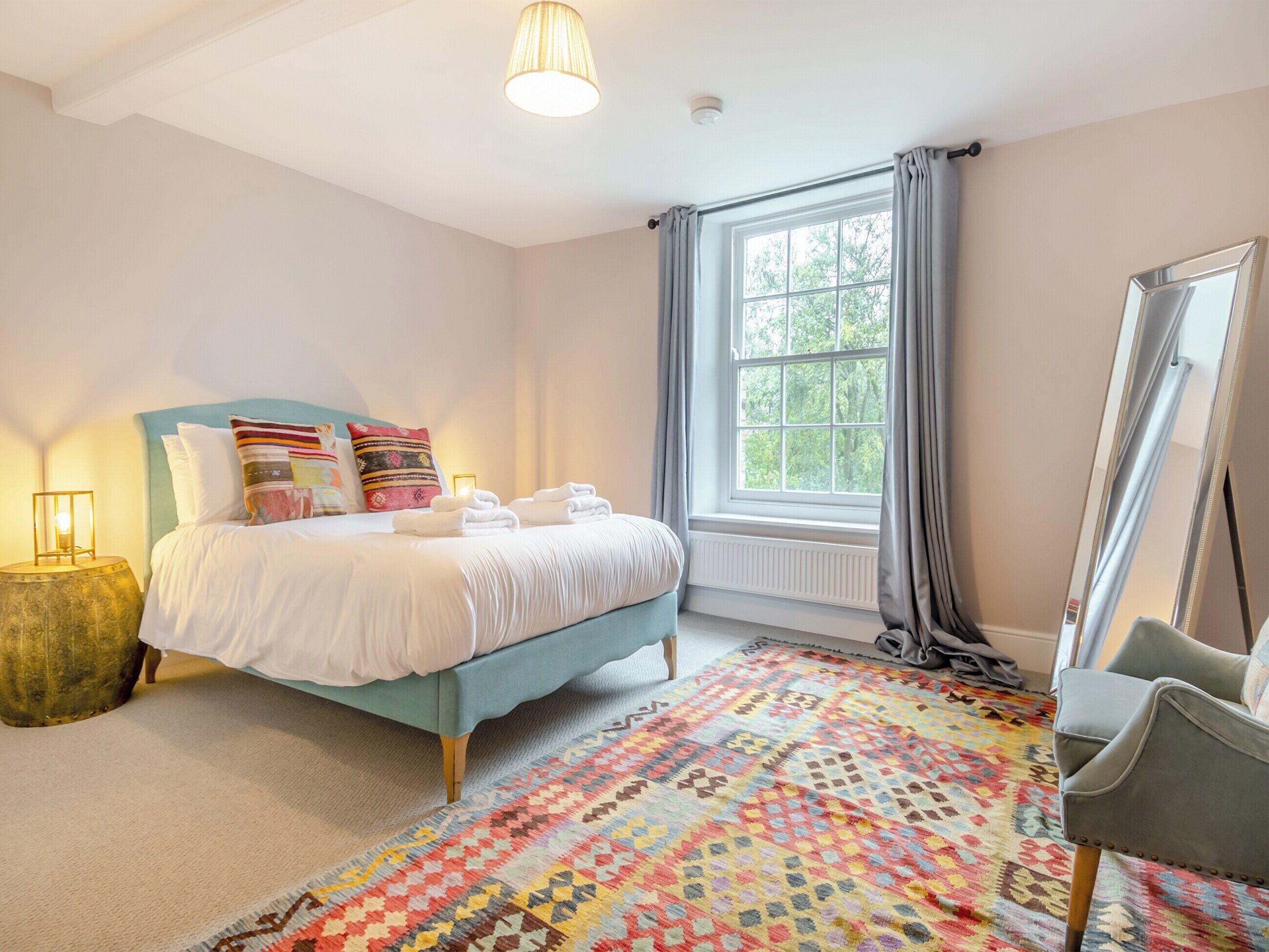 Ein Schlafzimmer mit Bett, Fenster, Spiegel und einem Teppich mit Muster.
