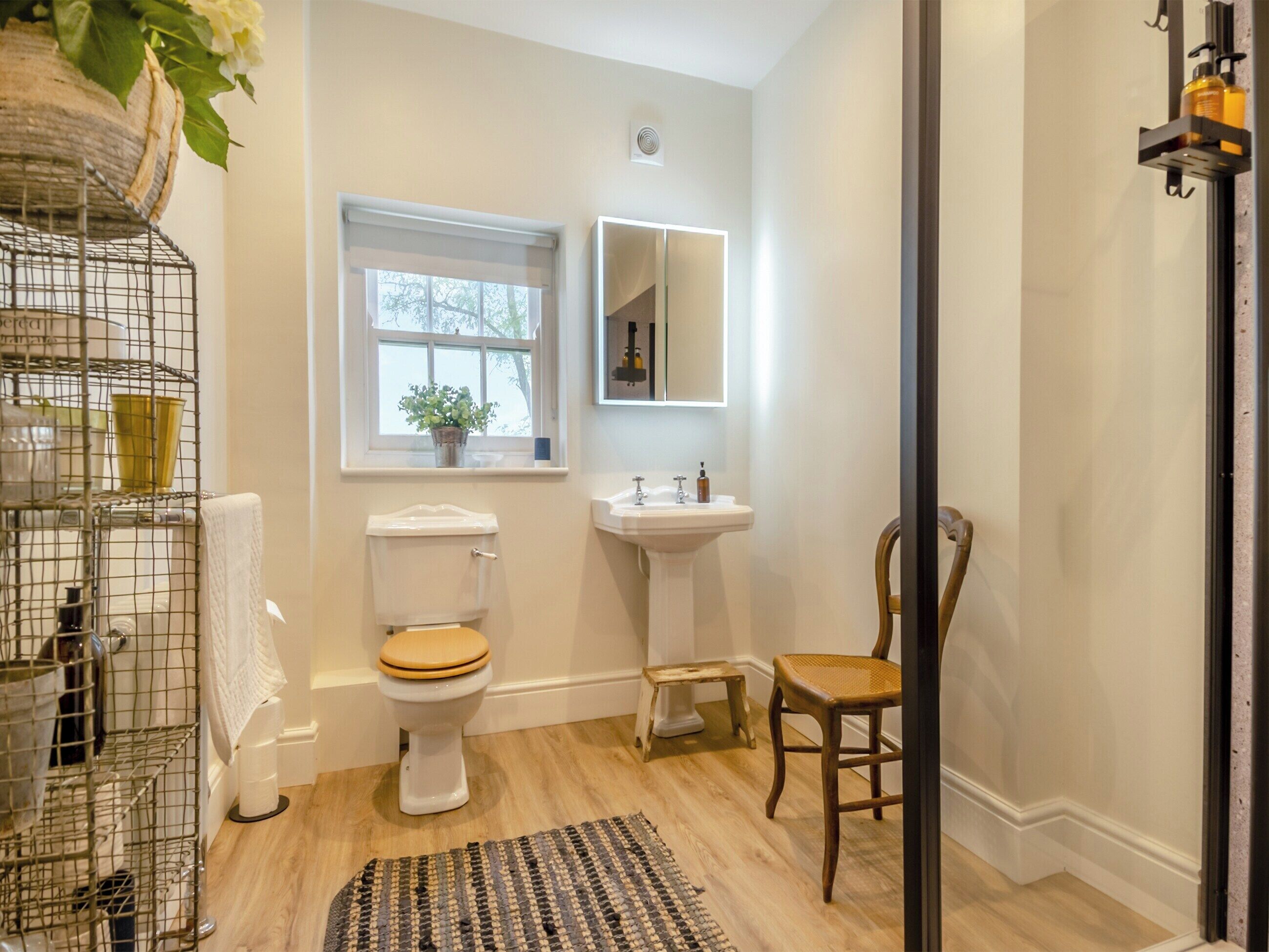 A bathroom with a toilet, sink, and chair.