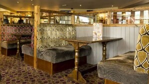 Un restaurante acogedor con cabinas de madera, una alfombra estampada y una zona de bar al fondo.