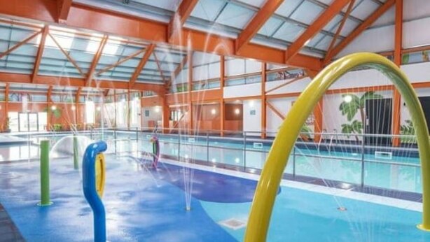 Una piscina interior con estructuras de juego coloridas y un techo alto con vigas a la vista.