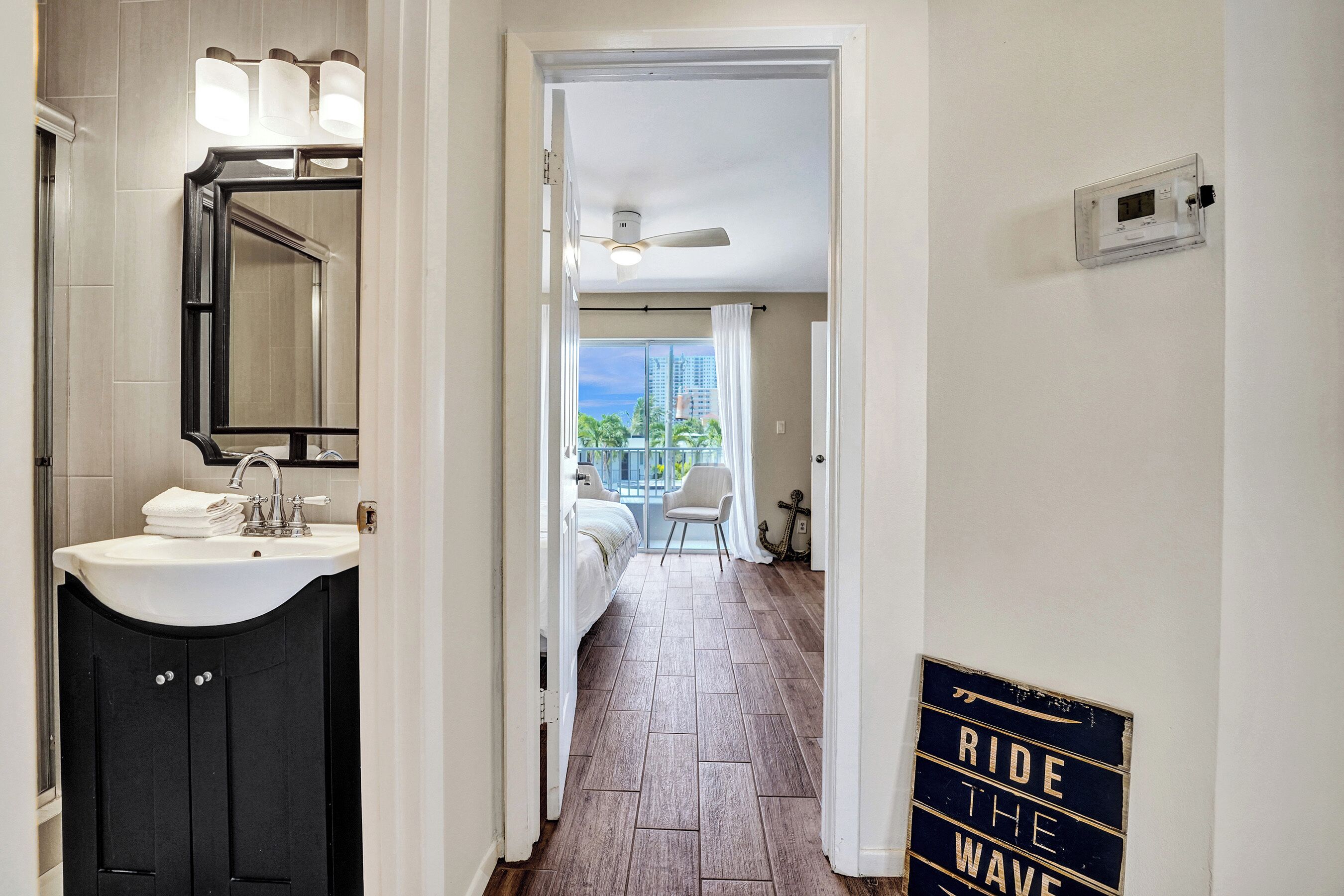 A hotel hallway with a bathroom on the left, a view of the balcony, and a sign on the wall.