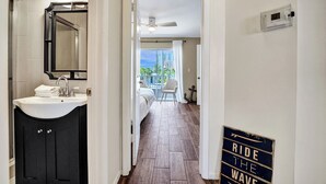Un couloir d’hôtel avec une salle de bain sur la gauche, une vue sur le balcon et un panneau sur le mur.