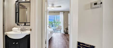A hotel hallway with a bathroom on the left, a view of the balcony, and a sign on the wall.
