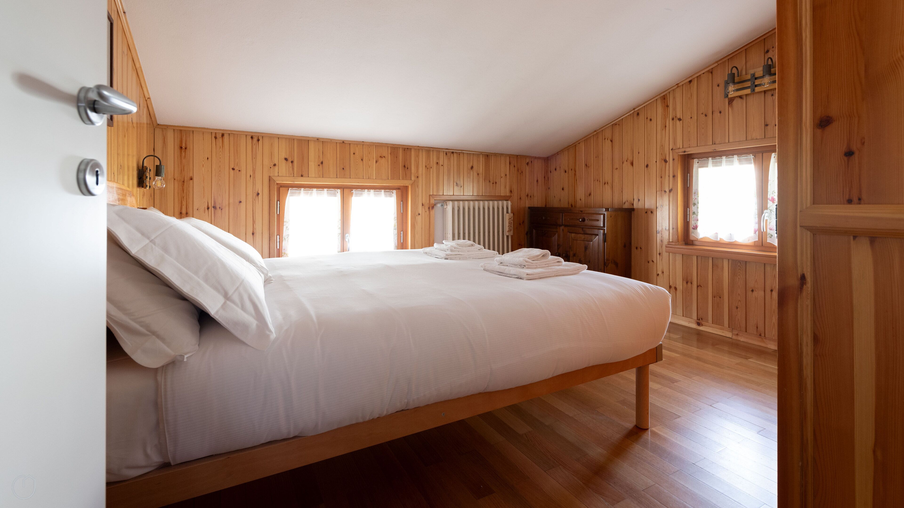 A wooden-paneled room with a bed, a radiator, and a window.