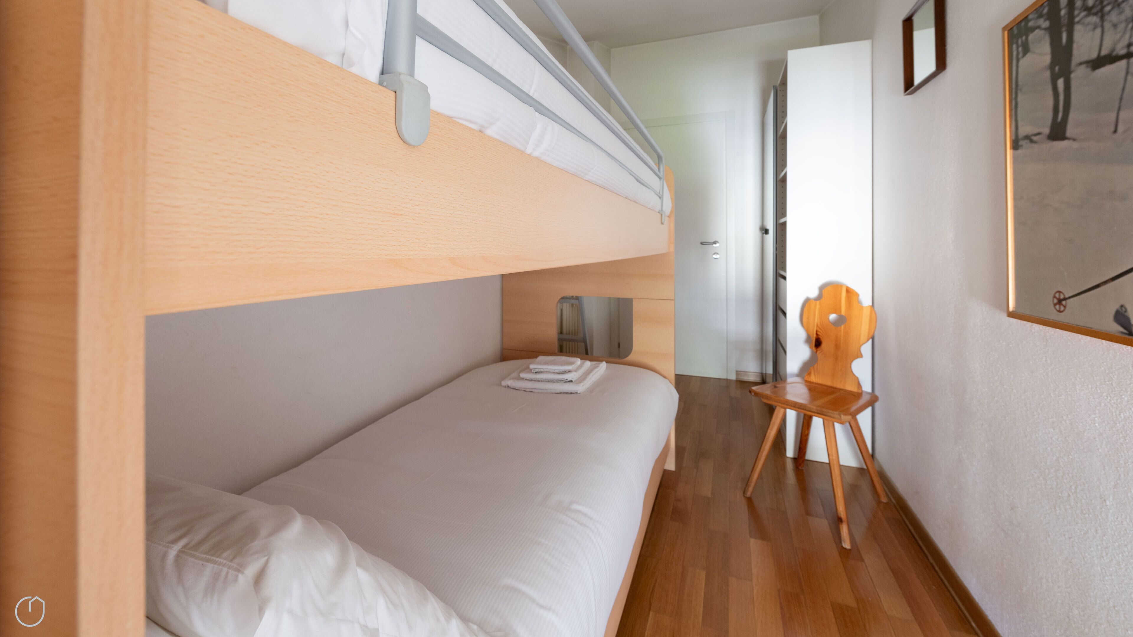 A bunk bed with a wooden headboard, a small wooden chair, and a framed picture on the wall.