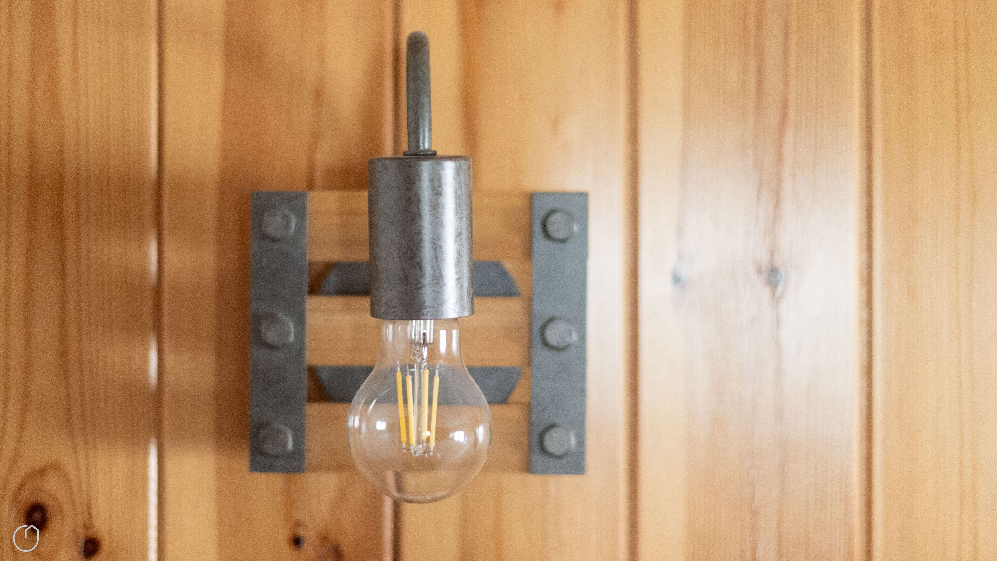 A clear glass bulb light fixture mounted on a wooden wall with metal brackets.