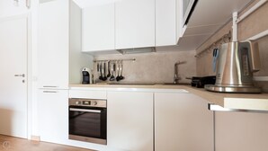 Eine moderne Küche mit weißen Schränken, einem eingebauten Ofen, einem Wasserkocher und verschiedenen Küchenutensilien, die an der Wand hängen.