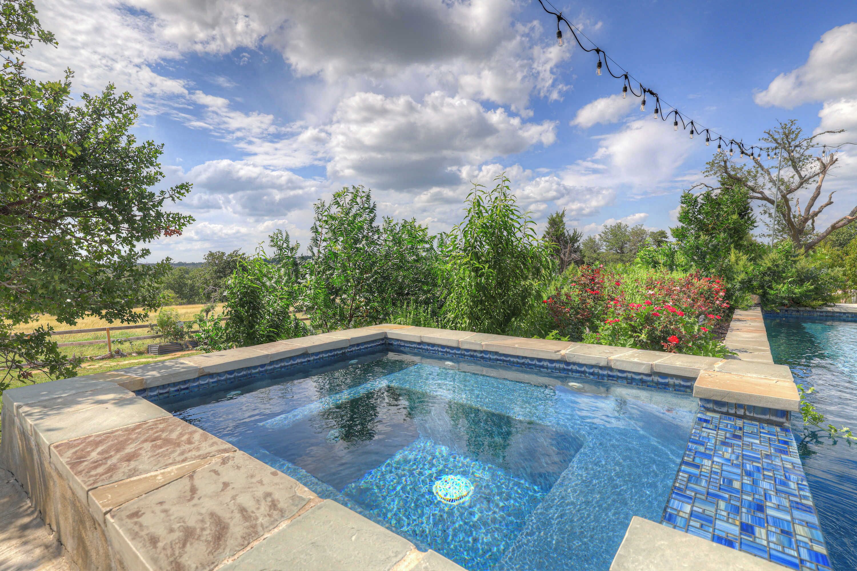 Una piscina rectangular con agua azul cristalina, rodeada por un borde de piedra y un borde con azulejos.
