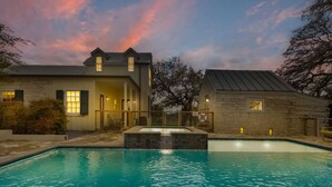 A pool area with a stone building, a second-story structure, and a sunset sky. - 7Cs Sunset Valley Ranch (Fredericksburg)