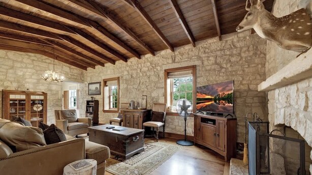 A rustic interior with stone walls, wooden beams, a fireplace, and a mounted deer head. - 7Cs Sunset Valley Ranch (Fredericksburg)
