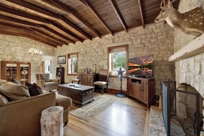 A rustic interior with stone walls, wooden beams, a fireplace, and a mounted deer head. - 7Cs Sunset Valley Ranch (Fredericksburg)