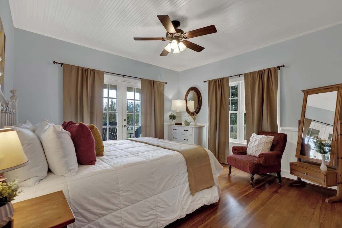 A bedroom with a bed, a chair, a dresser, a mirror, and a ceiling fan.