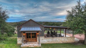 A rustic building with a covered outdoor seating area and a stone foundation. - Sunset Valley Ranch (Fredericksburg)