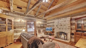 A rustic interior with exposed wooden beams, a stone fireplace, a sofa, and a dining table. - Sunset Valley Ranch (Fredericksburg)