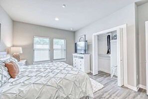 A bedroom with a bed, a dresser, a television, and a closet. - The Ricardo (Fredericksburg)