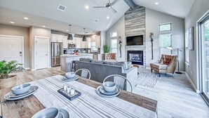 Amplia sala de estar con una mesa de comedor para cuatro, una chimenea y una cocina moderna al fondo.