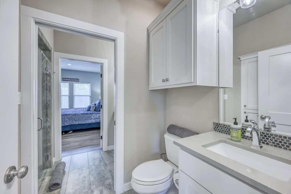 Une salle de bain avec des toilettes blanches, un lavabo doté d’un distributeur de savon et un miroir au-dessus du lavabo.