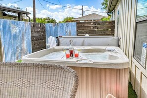 A hot tub with two drinks, a wicker chair, and a wooden fence in the background. - The Ricardo (Fredericksburg)