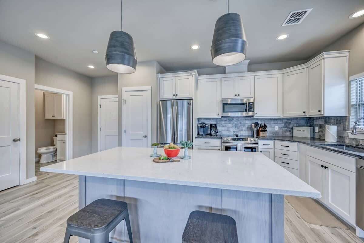 A modern kitchen with white cabinets, a large island, stainless steel appliances, and pendant lighting.