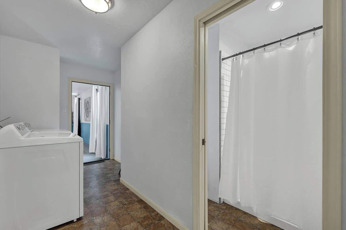Un lavadero con lavadora, piso de baldosas y una puerta que da a otra habitación.