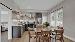 A modern kitchen with a central island, built-in appliances, and a dining area with wooden chairs. - The Grove Combo (Fredericksburg)