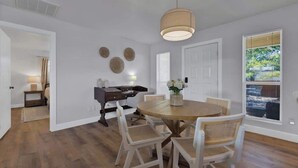 A dining area with a round table, white chairs, a hanging light fixture, and a window with blinds. - Weitz Retreat (Fredericksburg)
