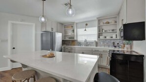 A modern kitchen with white cabinetry, a central island, and pendant lighting. - Weitz Retreat (Fredericksburg)