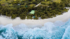 An aerial view of a beach with a small cluster of buildings surrounded by dense palm trees. - Suffix Retreat - Stay, Dive & Explore Fuvahmulah (Fuvahmulah)