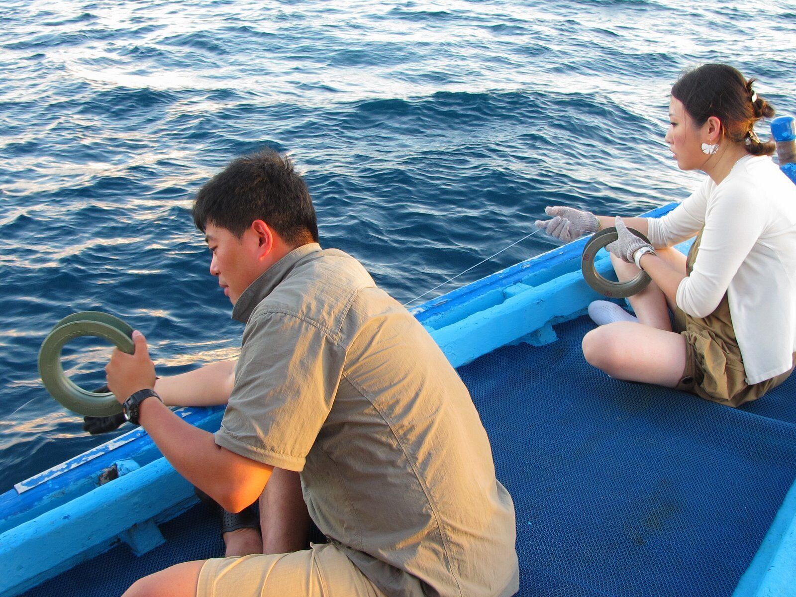 Dos personas en un bote, uno manejando un timón y otro sosteniendo una cuerda.