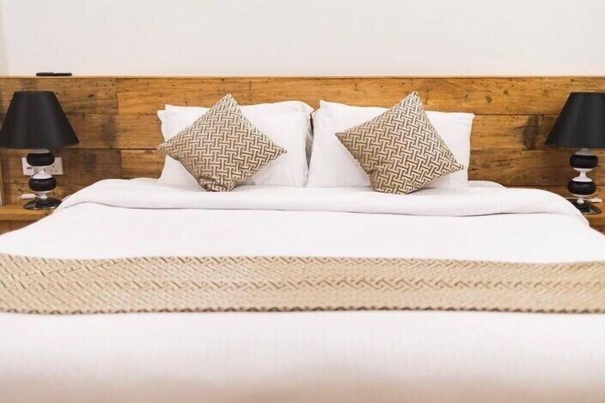 Un lit avec du linge de lit blanc, deux coussins à motifs et un plaid tissé.