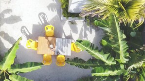 A top-down view of a dining area with a wooden table and yellow chairs, surrounded by large green banana leaves. - Suffix Retreat - Stay, Dive & Explore Fuvahmulah (Fuvahmulah)