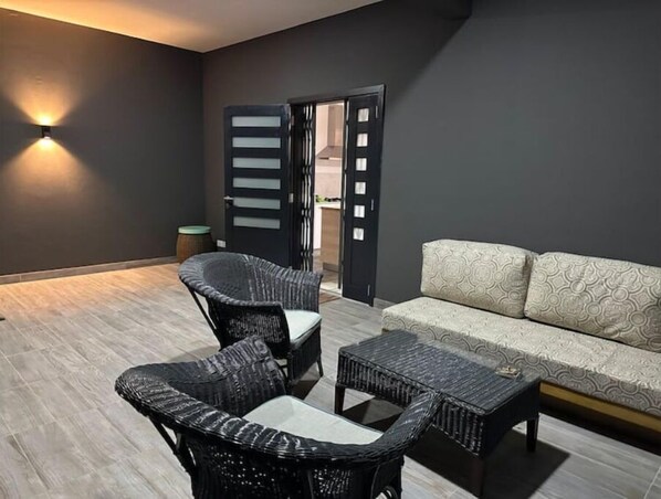 A modern living room with a dark wall, a sofa, two wicker chairs, and a coffee table.