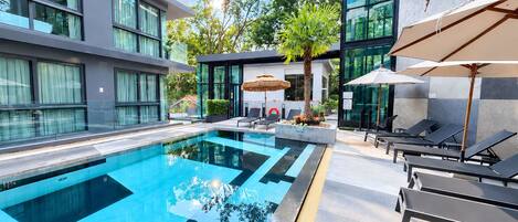 A modern hotel with a swimming pool, lounge chairs, and a glass facade.