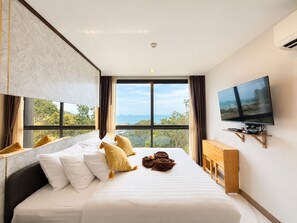 A hotel room with a bed, a television, and a view of the sea.