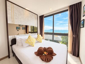 A hotel room with a large bed, a view of the sea, and a marble headboard.