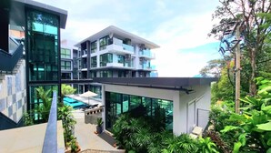Un edificio moderno de varios pisos con fachada de vidrio, piscina exterior y abundante vegetación.