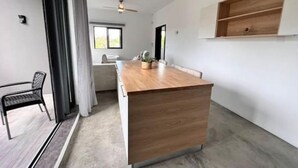 Ett modernt kök med en köksö i trä, en matplats med stolar och utsikt över utomhusmiljön.