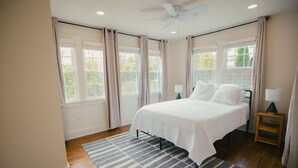 Un dormitorio con cama, ventilador de techo, mesita de noche y ventana con cortinas.