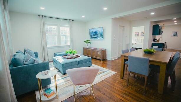 Una sala de estar moderna con un sofá, un reposapiés y un comedor con una mesa y sillas.