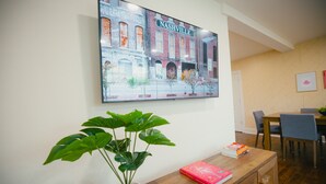 Una habitación con una fotografía grande enmarco de un edificio que dice "Nashville", una planta en maceta, una mesa de madera con un libro, y un comedor con sillas y una mesa.