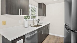 Une cuisine moderne avec des meubles en bois foncé, des plans de travail blancs, des appareils électroménagers en acier inoxydable et une fenêtre équipée de stores.